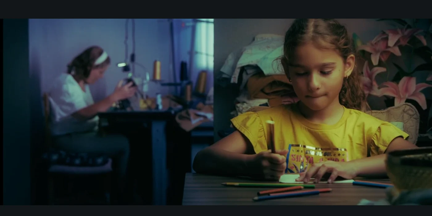 Menina desenhando e uma mulher trabalhando ao fundo em uma cena do filme